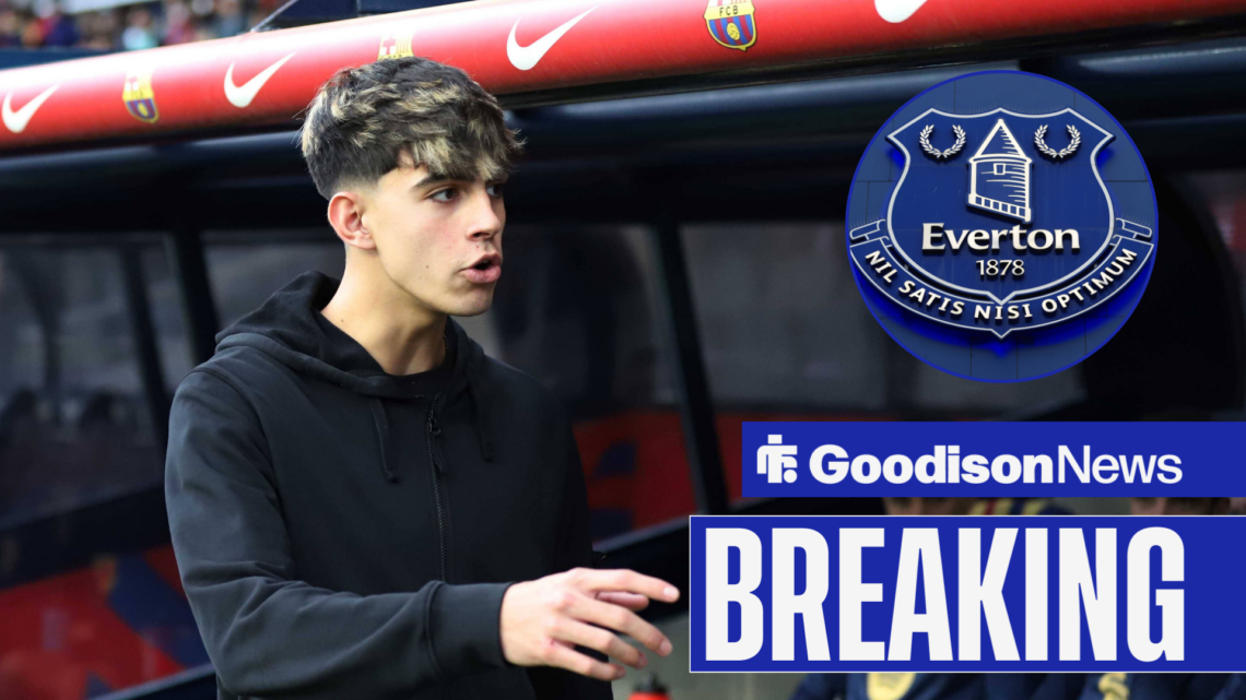Barcelona midfielder Marc Bernal chats by his team's dug out. To the right of him is an Everton crest.