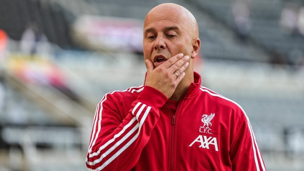 Arne Slot rubbing his mouth in red Liverpool tracksuit